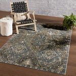 Blue and gold medallion rug styled under a wood chair with black woven straps and wood side table