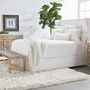 Styled bedroom scene with woven rope bench positioned at foot of bed on plush white rug