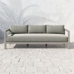 Outdoor sofa shown outdoors on stone patio with sunlight and palm shadow on white wall