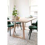 Dining table styled with green velvet chairs and white decorative vases on light textured rug in bright room