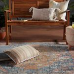 Lumbar pillow on patterned rug in an outdoor seating area with wooden bench and other cushions