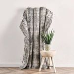 Rug draped against white wall with light wood stool and green plant for room context