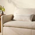 Harvey White Pillow placed on a cream-colored sofa with floral decor in soft natural lighting