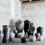 Multiple black and gray vases with varying forms grouped in rustic room with exposed brick
