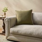 Pillow styled on beige couch in living room setting with side table and decorative vase