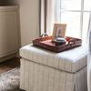Ottoman styled in room corner with window light, wooden tray on top holding decor items