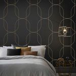 Bedroom setting showcasing black wallpaper with gold geometric curves behind bed with neutral pillows and modern lighting