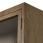 Close-up of cabinet door corner with glass panel and metal hinge hardware on drifted oak wood