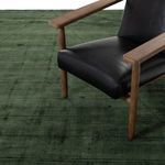 Green rug beneath black leather chair legs and wooden armrest in modern styled room