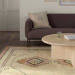 Rug corner under round table with sofa in background, showing medallion patterns.