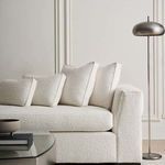 Front angled view in room setting showing textured upholstery and multiple cushions with a standing lamp nearby