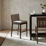 Wilmington Stool near black table and rustic decorative bowl on beige patterned rug in softly lit dining room