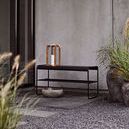 Storm lantern placed on black metal bench in minimalist outdoor gravel area next to planter with greenery