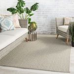 Rug styled in modern indoor setting with wicker sofas, plants, and white brick wall backdrop