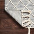 Sawyer Teal Rug corner lifted to reveal flat woven back and fringe knots on dark hardwood flooring
