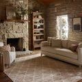 Townes Pebble rug styled in a rustic living room with stone walls, wooden ceiling, couch, and armchair