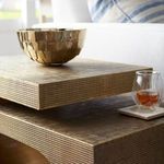 Detail view of layered top surfaces and textured brass finish with glass of beverage on coaster beside sofa