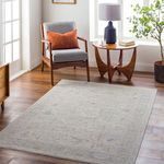 Rug placed in bright living room with gray chair, orange pillow, wooden side table, and floor lamp
