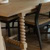 Angle showing table top grain pattern and leg detail with woven chairs under the table