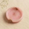 Side angled view showing depth and brown veining inside the pink alabaster round tray on beige fabric background