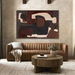 Repeated horizontal painting above tufted leather sofa with beige throw pillow and round wooden table