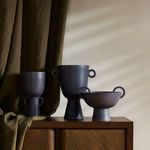 Three black vases of varying sizes styled on a wooden cabinet with fabric backdrop under natural light