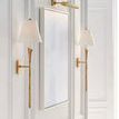 Picture light mounted above tall plain rectangular mirror flanked by brass wall sconces with white shades
