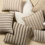 Multiple pillows in varying earthy tones and stripe patterns arranged on a textured cream carpet