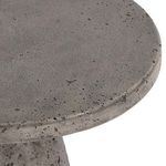 Dark gray outdoor accent table with a curved base and round textured concrete top with subtle gleam