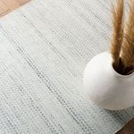 Close-up of rug surface with white ceramic vase holding dried pampas grass on light wooden floor