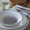 Top view of white and blue rim Beja salad bowl stacked on plates with bread and glass on rustic wooden table