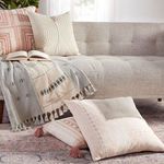 Close-up of rug under sofa with layered pink and cream pillows with tassels and coordinating throw blanket