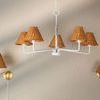 Full view of chandelier with five white arms and rattan shades with two brass sconces