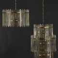 Chandeliers shown in dim lighting against dark wall highlighting clear textured glass bars and warm brass