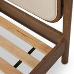 Close-up detail where ivory fabric upholstery meets rounded smoked oak frame on headboard
