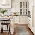 Runner rug placed in kitchen with white cabinetry, wood floor, and black chair under island