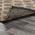 Corner of rug lifted to reveal backing texture and flexibility on gray wood floor