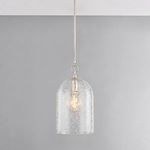 Pendant lit and suspended in front of gray wall highlighting the floral etching with warm glow