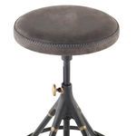 Close-up on round leather seat showing contrast stitching and brass height adjustment knob