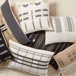 Several cream, black, and tan tribal pattern pillows displayed together on a beige carpet