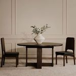 Two Kerr dining chairs flanking round dining table with decorative vase in a neutral-toned room