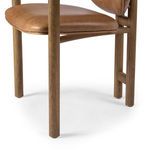 Detailed view of tapered wooden front chair leg and caramel leather seat cushion edge