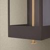 Close-up showing lower corner of dark frame and brass rod with textured wall background