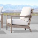Side view of Laguna Club Chair in natural driftwood finish with beige cushions beside concrete ledge and mountain backdrop