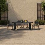 Outdoor setting with oval teak table and four woven black and natural wood chairs against stucco wall