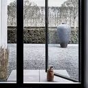 Camou Door Stopper placed on tiled floor holding open glass door with outdoor gravel and large vase in background