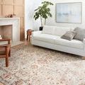 Estelle Ivory Rust rug in a living room setting with white sofa, wooden chair, plant, and artwork