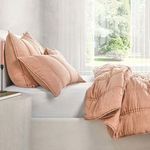 Side angled view of quilt draped off bed edge highlighting soft softness and layered pillows