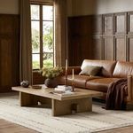 Isaac Coffee Table staged in living room with leather sofa, area rug, and wood paneled walls