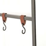 Close-up of single gunmetal S-hook attached to brown leather strap on frame